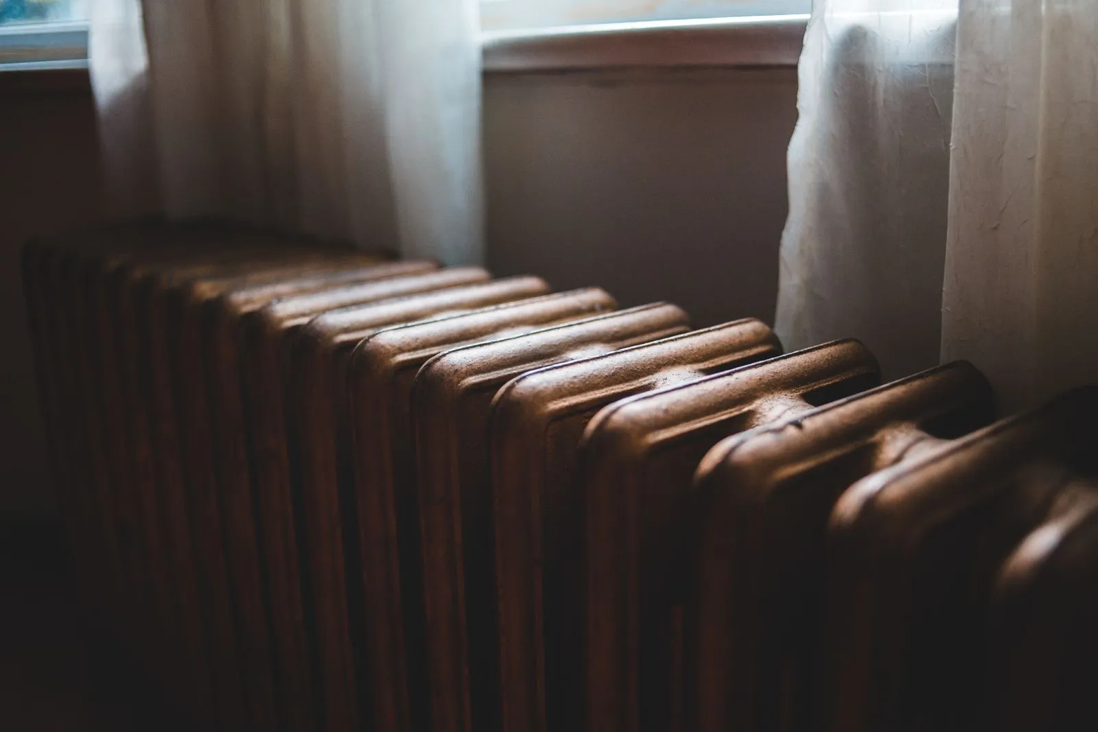 Old cast-iron radiator beneath a window with sheer curtains
